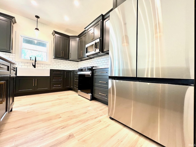 kitchen with a sink, stainless steel appliances, light wood-type flooring, backsplash, and pendant lighting