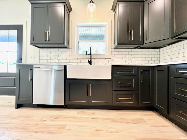 kitchen featuring a sink, light countertops, light wood-type flooring, tasteful backsplash, and stainless steel dishwasher