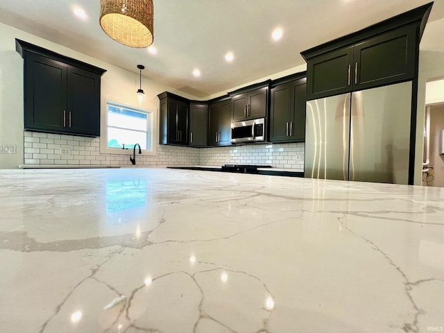kitchen with light stone countertops, tasteful backsplash, a sink, hanging light fixtures, and stainless steel appliances