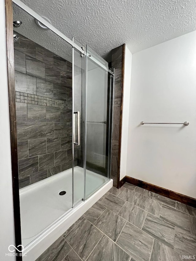 bathroom featuring a textured ceiling, baseboards, and a stall shower