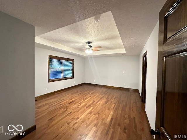 spare room featuring a ceiling fan, a textured ceiling, baseboards, dark wood-style floors, and a tray ceiling