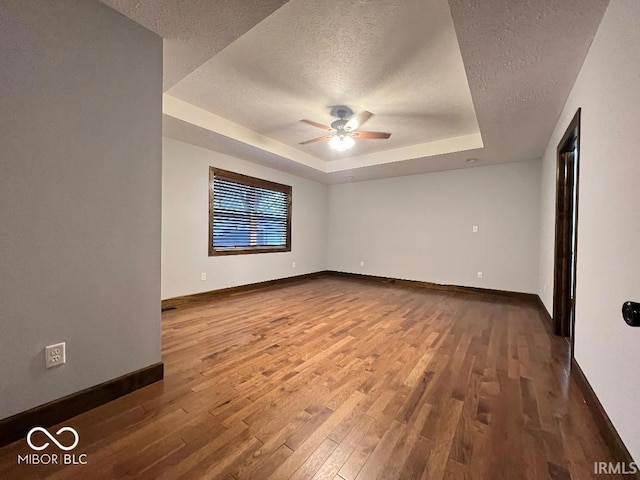 spare room with a ceiling fan, a textured ceiling, wood finished floors, a raised ceiling, and baseboards