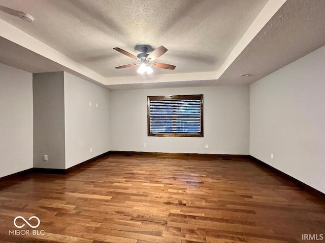 unfurnished room with a raised ceiling, a textured ceiling, ceiling fan, and wood finished floors