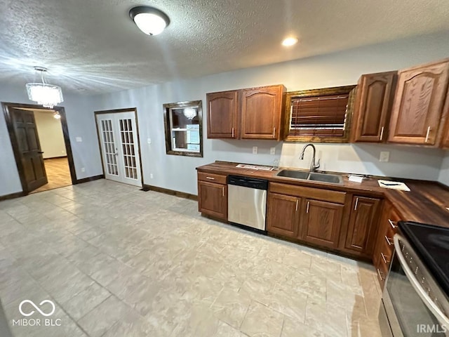 kitchen with dark countertops, a sink, a textured ceiling, stainless steel appliances, and baseboards