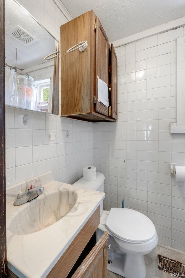 full bath featuring tile walls, vanity, toilet, and visible vents