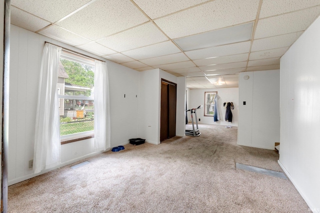 carpeted empty room with visible vents and a drop ceiling
