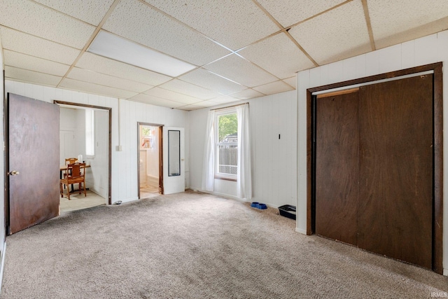 unfurnished bedroom featuring wooden walls, a drop ceiling, carpet, and a closet