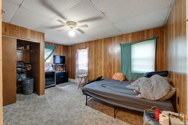 carpeted bedroom featuring wooden walls, ceiling fan, a drop ceiling, and beverage cooler