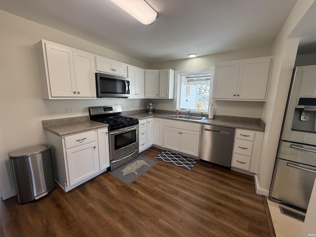 kitchen with dark countertops, dark wood finished floors, a sink, stainless steel appliances, and white cabinetry