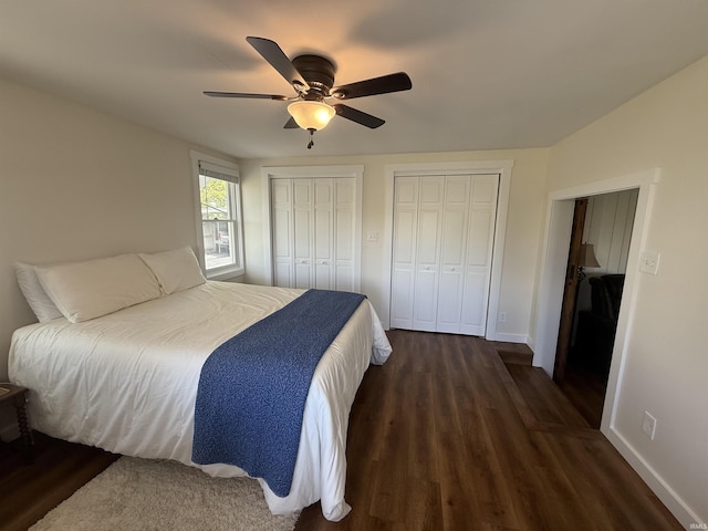 bedroom featuring dark wood-type flooring, a ceiling fan, baseboards, and two closets