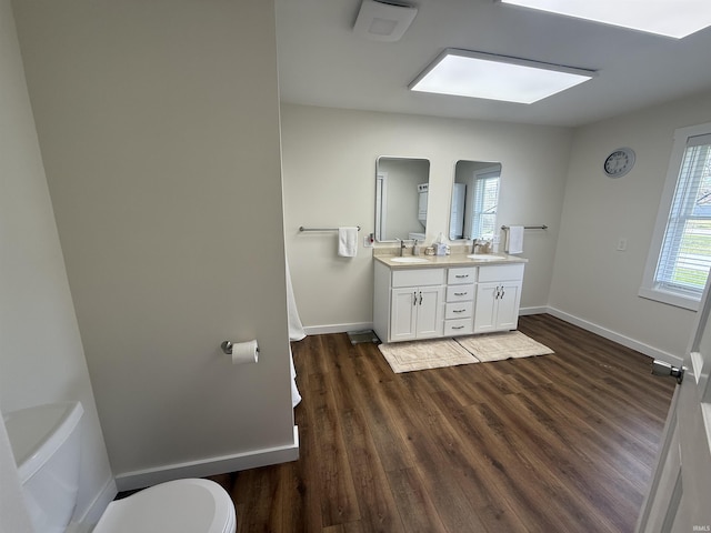 bathroom with baseboards, double vanity, wood finished floors, and toilet