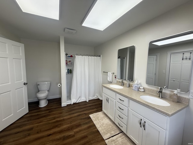 bathroom featuring double vanity, a sink, wood finished floors, and toilet