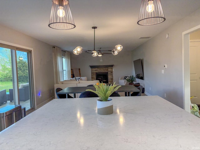 dining area featuring an inviting chandelier, baseboards, a stone fireplace, and visible vents