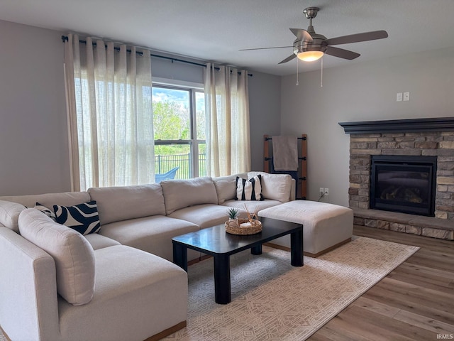 living area featuring ceiling fan, a stone fireplace, and wood finished floors