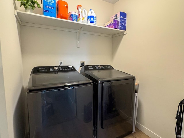 clothes washing area with separate washer and dryer, laundry area, baseboards, and wood finished floors