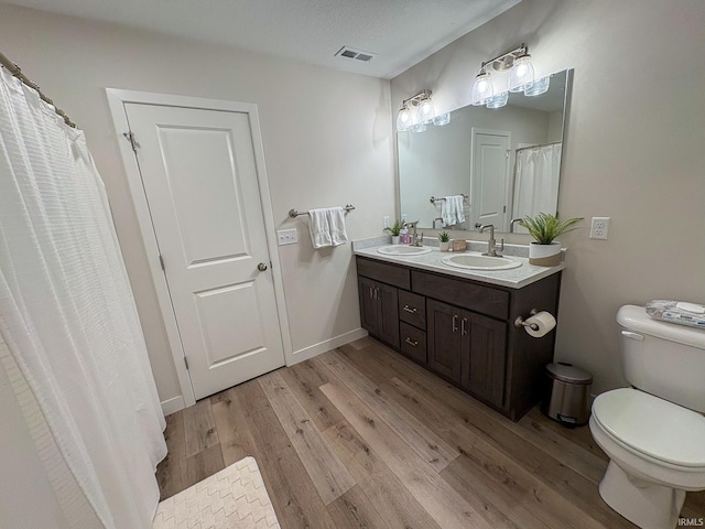 bathroom featuring toilet, visible vents, a sink, and wood finished floors