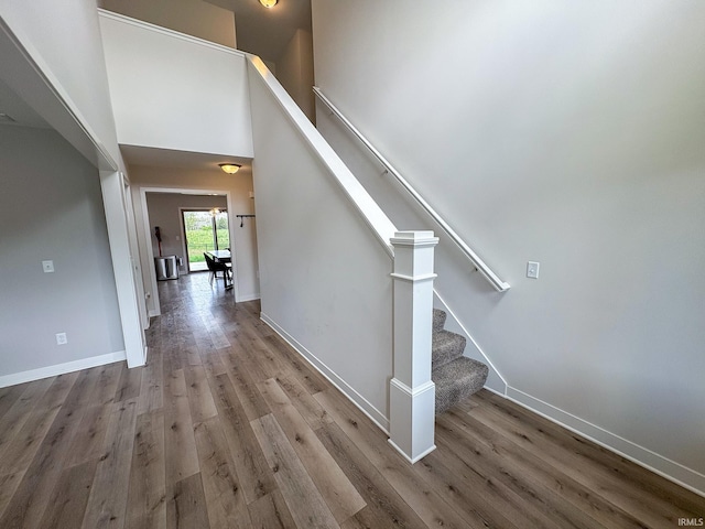 stairway with baseboards, a towering ceiling, and wood finished floors