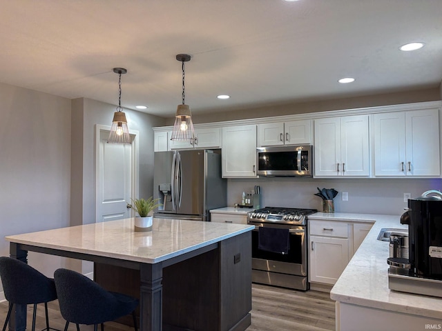 kitchen with white cabinets, appliances with stainless steel finishes, a breakfast bar area, light wood-type flooring, and a kitchen island