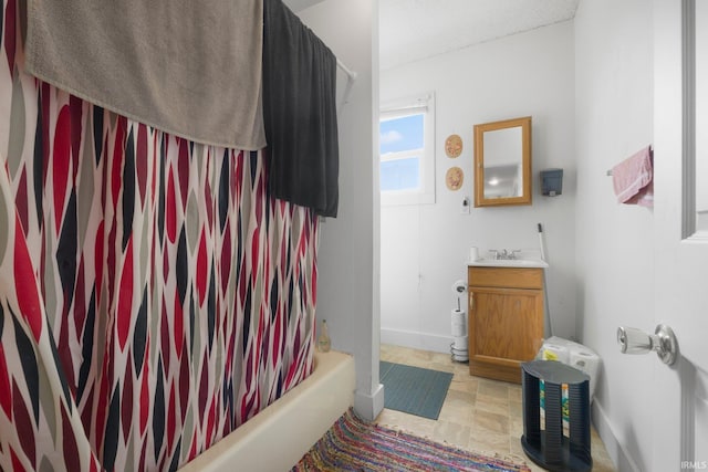 full bath featuring baseboards, stone finish flooring, shower / bath combination with curtain, and vanity