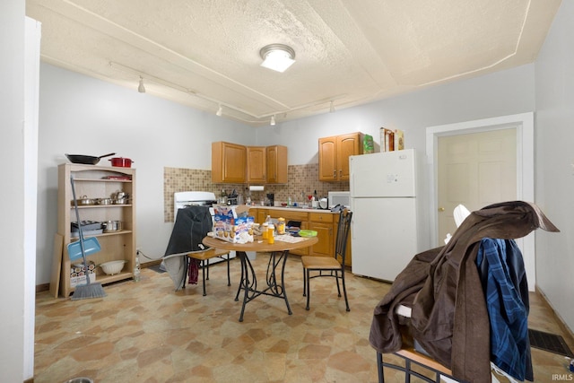 kitchen with track lighting, decorative backsplash, white appliances, stone finish floor, and light countertops