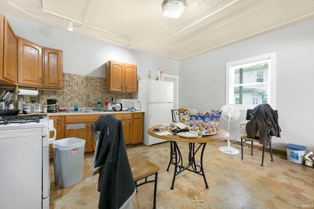 kitchen featuring a sink, white appliances, light countertops, rail lighting, and backsplash
