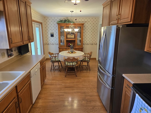 kitchen with white dishwasher, hanging light fixtures, stainless steel fridge, wallpapered walls, and light wood-type flooring