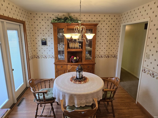 dining room with dark wood-style flooring, wallpapered walls, and an inviting chandelier