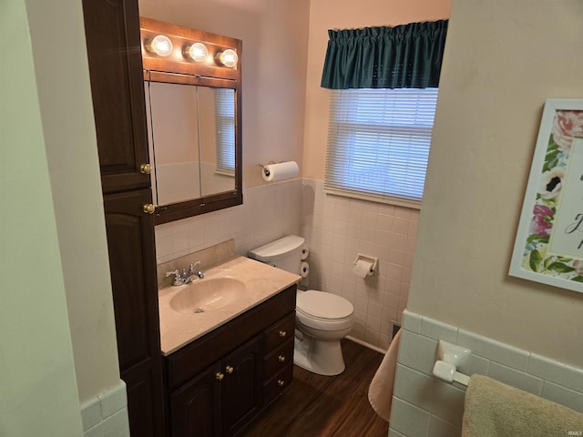 bathroom featuring tile walls, wood finished floors, a wainscoted wall, vanity, and toilet