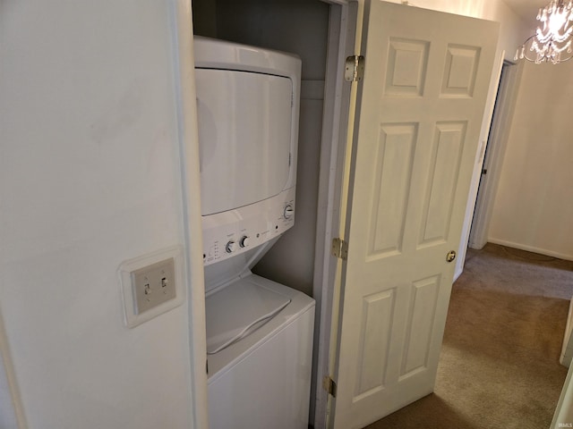 laundry room featuring laundry area, an inviting chandelier, stacked washer / dryer, and dark carpet