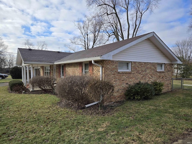 view of side of home featuring a lawn, brick siding, fence, and a shingled roof