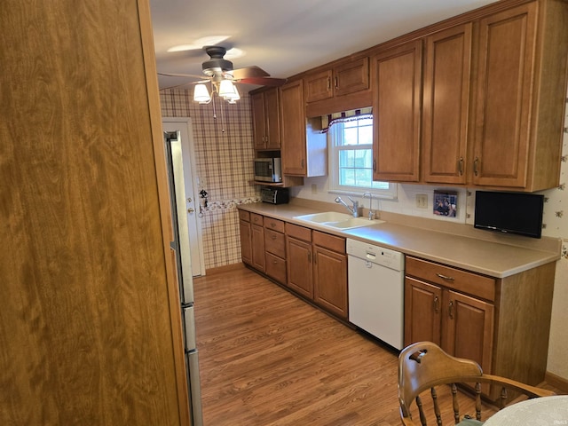 kitchen with a sink, dishwasher, wallpapered walls, stainless steel microwave, and light wood-type flooring