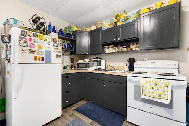 kitchen featuring open shelves, a sink, light countertops, white appliances, and light wood-style flooring