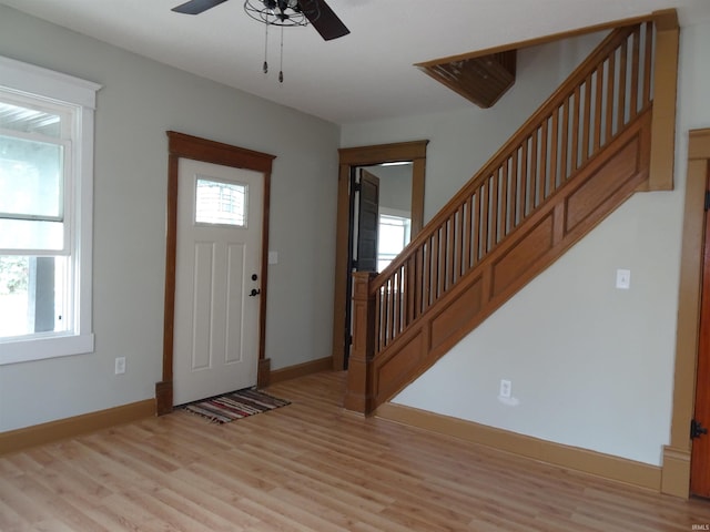 entryway featuring baseboards, light wood-type flooring, a ceiling fan, and stairs