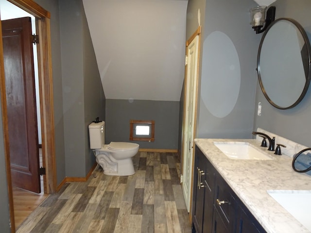 full bath featuring double vanity, wood finished floors, a sink, toilet, and lofted ceiling