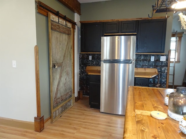 kitchen featuring tasteful backsplash, light wood-type flooring, a barn door, freestanding refrigerator, and butcher block counters