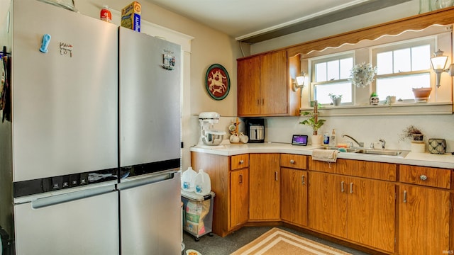 kitchen with freestanding refrigerator, brown cabinetry, a sink, and light countertops