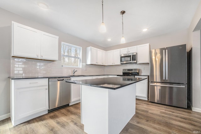 kitchen with dark countertops, wood finished floors, a sink, stainless steel appliances, and white cabinetry