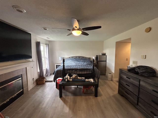 bedroom with freestanding refrigerator, a ceiling fan, wood finished floors, and a tile fireplace