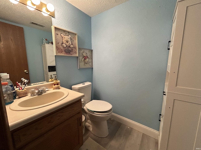 bathroom featuring visible vents, wood finished floors, toilet, baseboards, and a textured ceiling