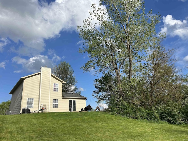 exterior space featuring a lawn, a chimney, and central air condition unit