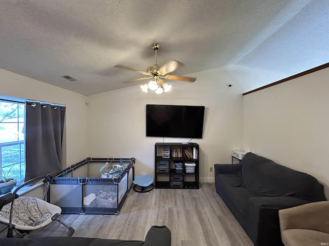 living area with wood finished floors, baseboards, ceiling fan, a textured ceiling, and vaulted ceiling