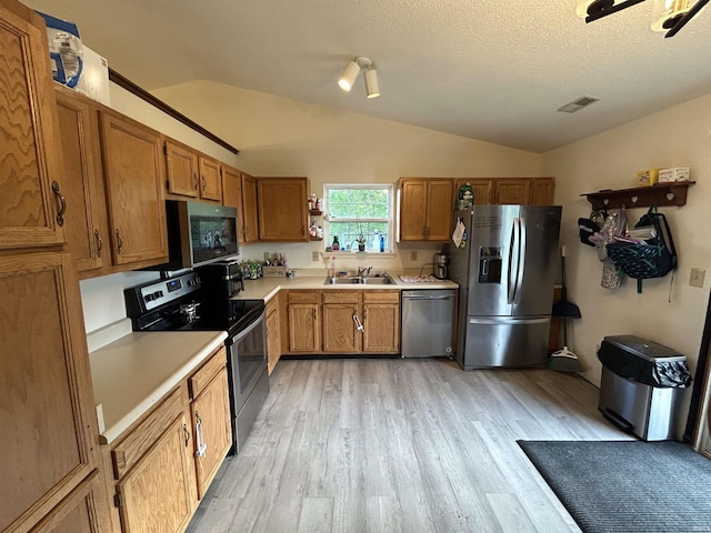 kitchen featuring lofted ceiling, light wood-style floors, light countertops, a sink, and stainless steel appliances