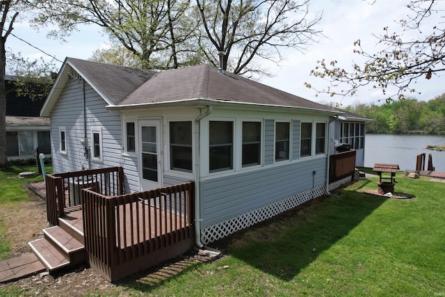 rear view of property with a shingled roof, a yard, and a deck with water view