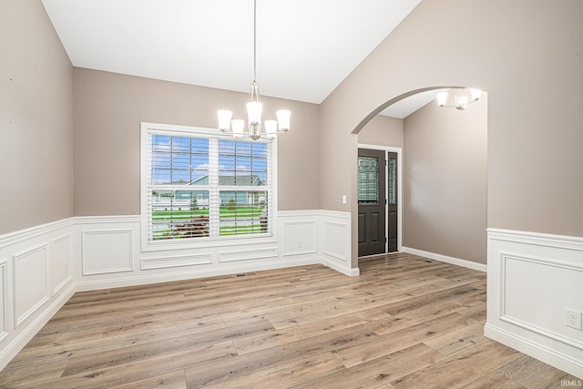 unfurnished dining area with arched walkways, an inviting chandelier, light wood-type flooring, and a wainscoted wall
