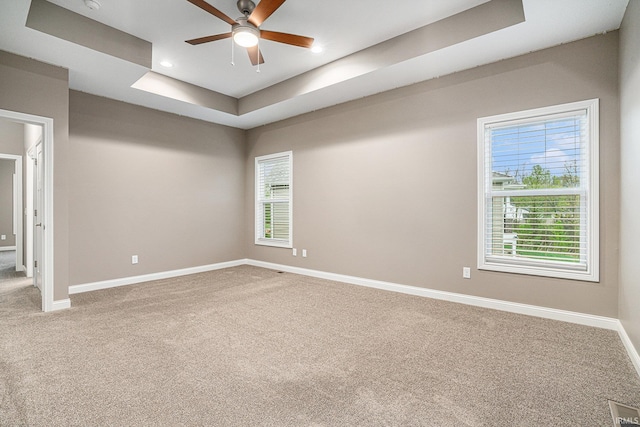 carpeted spare room with baseboards, ceiling fan, a tray ceiling, and visible vents