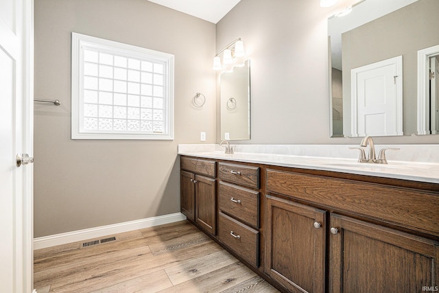 bathroom featuring a sink, double vanity, baseboards, wood finished floors, and visible vents