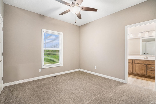 unfurnished bedroom featuring connected bathroom, light colored carpet, a ceiling fan, baseboards, and visible vents