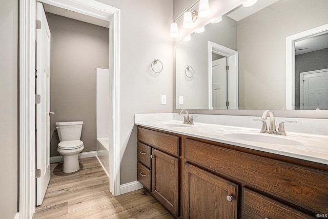 full bath featuring double vanity, a sink, wood finished floors, and toilet