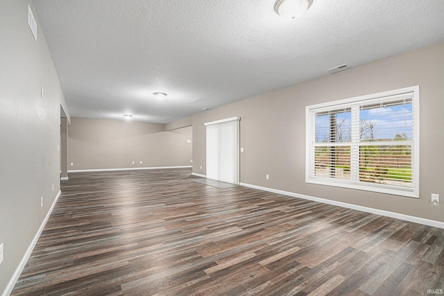 unfurnished room featuring baseboards, dark wood-style floors, a textured ceiling, and visible vents