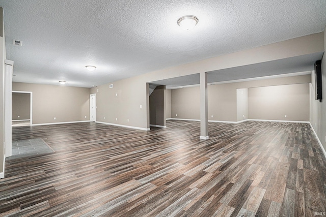 finished below grade area featuring baseboards, dark wood-style floors, a textured ceiling, and visible vents